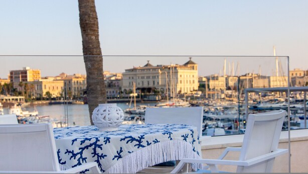 Une table recouverte d’une nappe blanche, agrémentée d’un vase décoratif, donnant sur une marina où l’on aperçoit des bateaux et des bâtiments en arrière-plan.