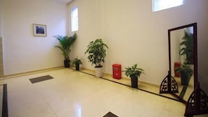 Eine geräumige Lobby mit Fliesenboden, Topfpflanzen, einem großen Spiegel und einem gerahmten Bild an der Wand.