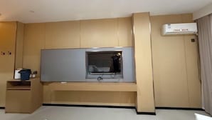 Ein modernes Hotelzimmer mit integriertem Fernseher, einem kleinen Schreibtisch und einer Wandklimaanlage.