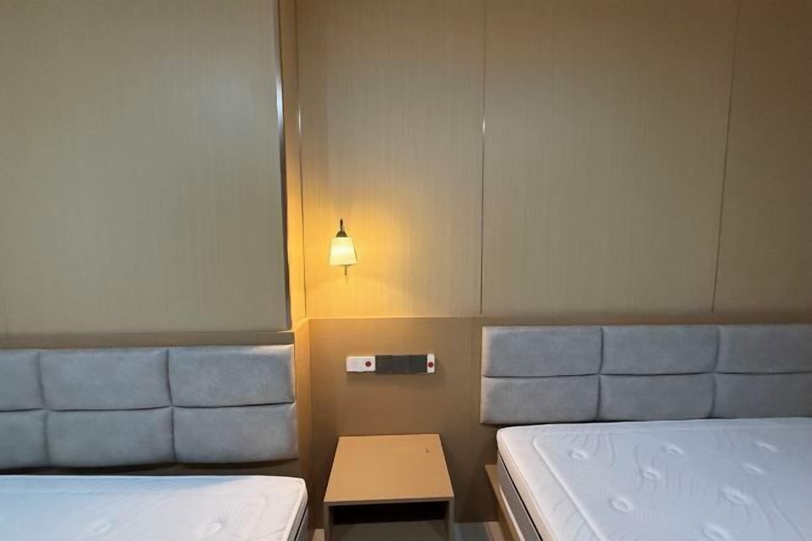 A hotel room with two beds, a small bedside table, and a wall-mounted light fixture.