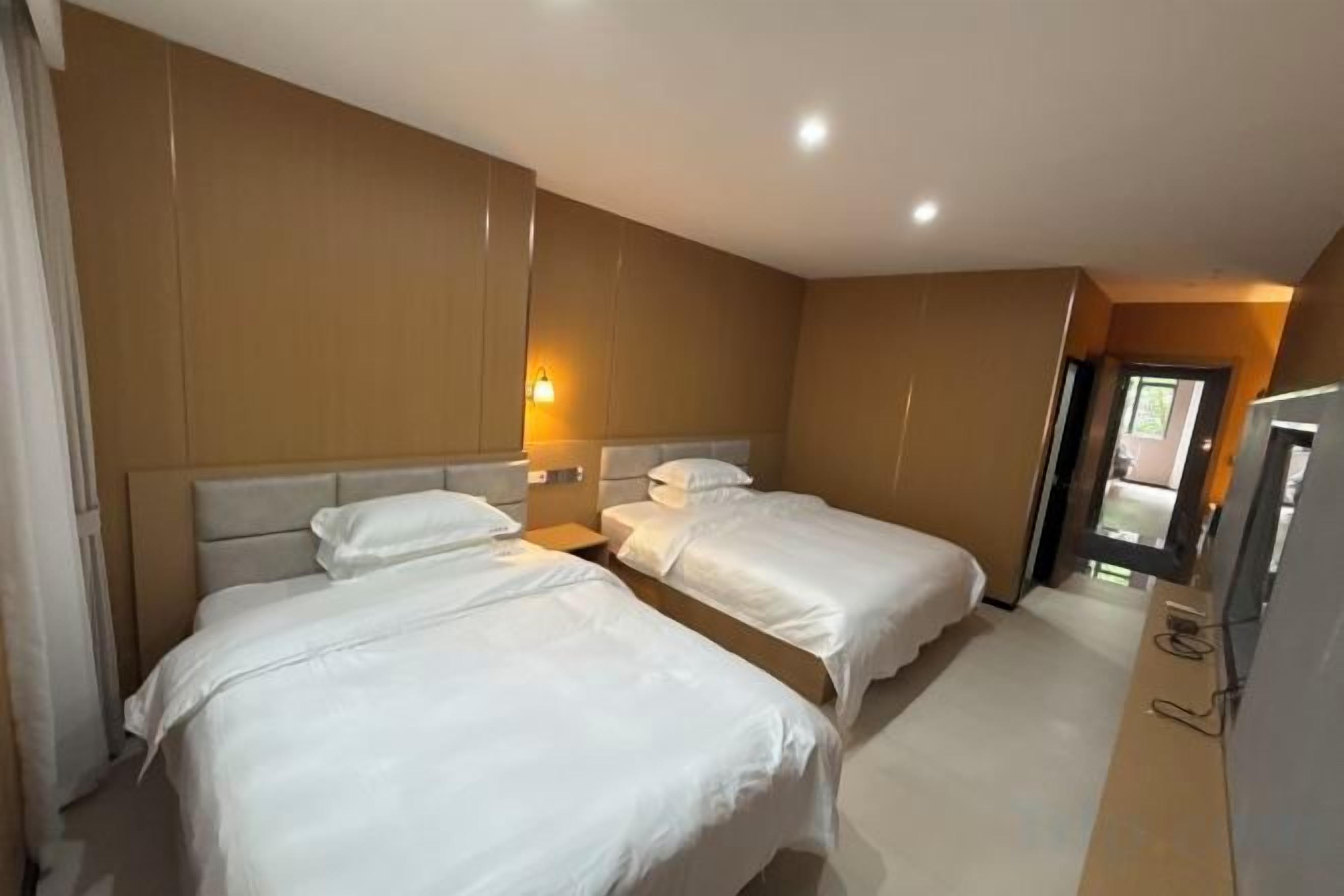 A hotel room with two beds, a bedside table, a TV, and a door leading to a balcony.