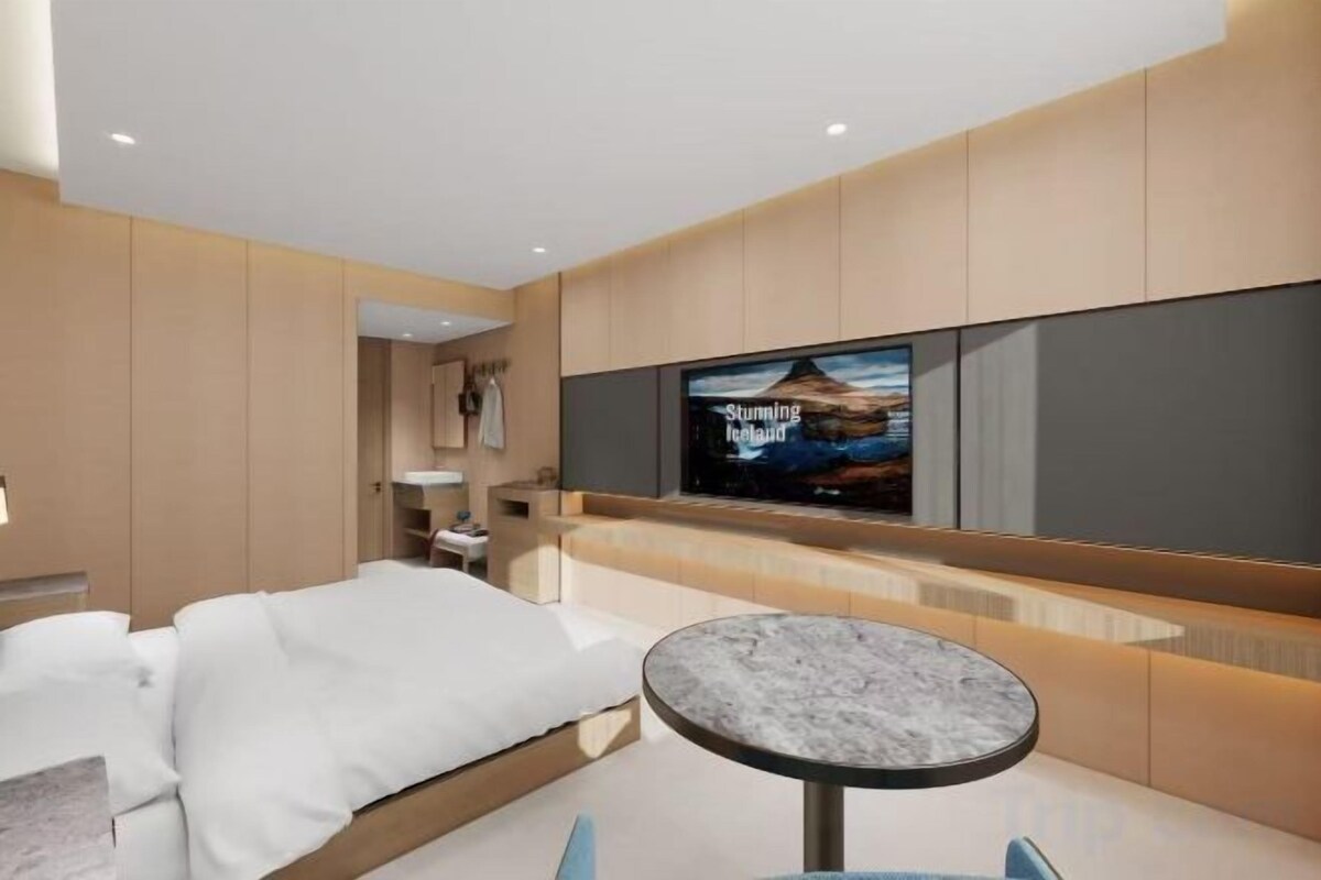 A modern hotel room with a bed, a television mounted on the wall, and a small round table.