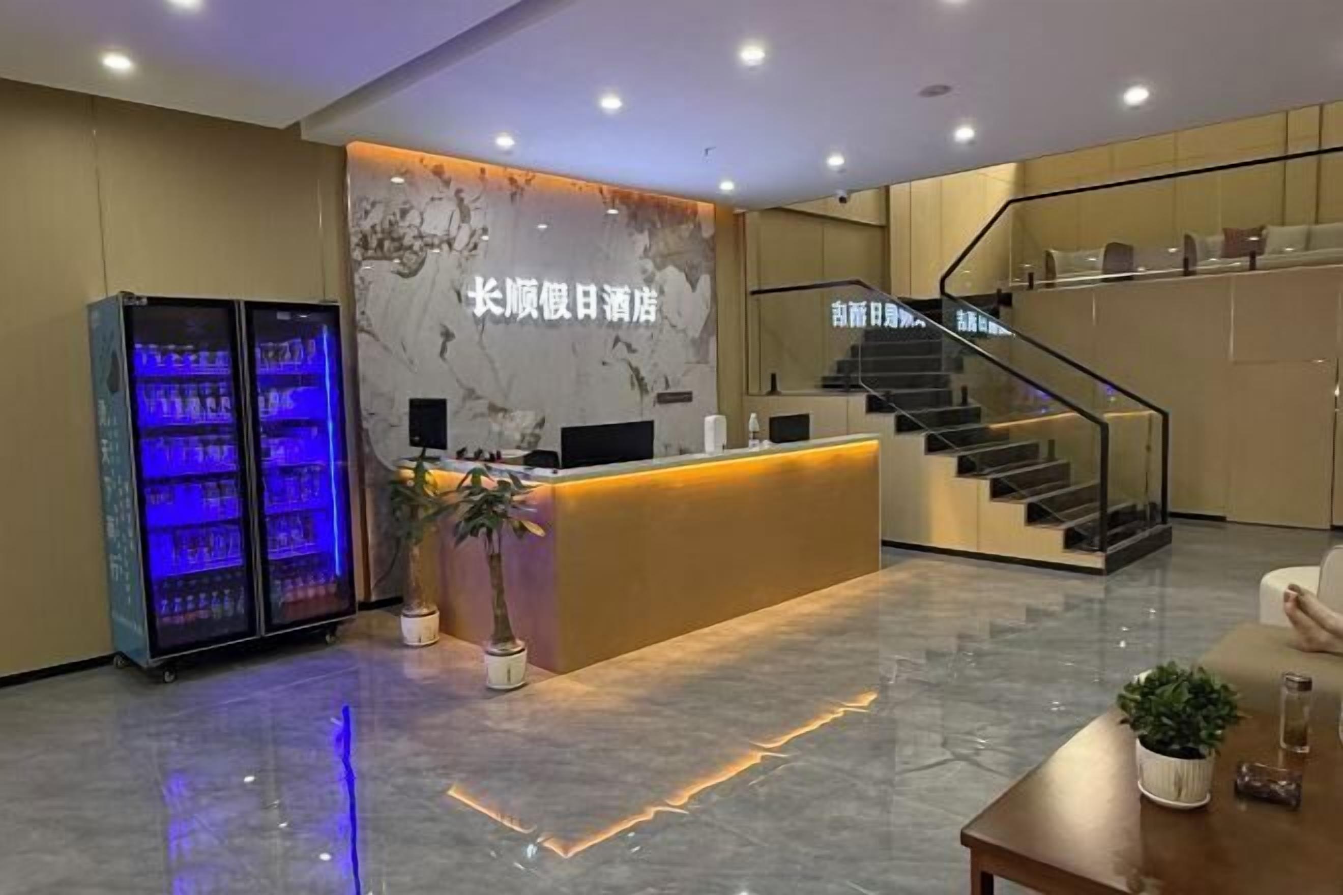A hotel reception area with a marble wall, a reception desk, a staircase, and a minibar.