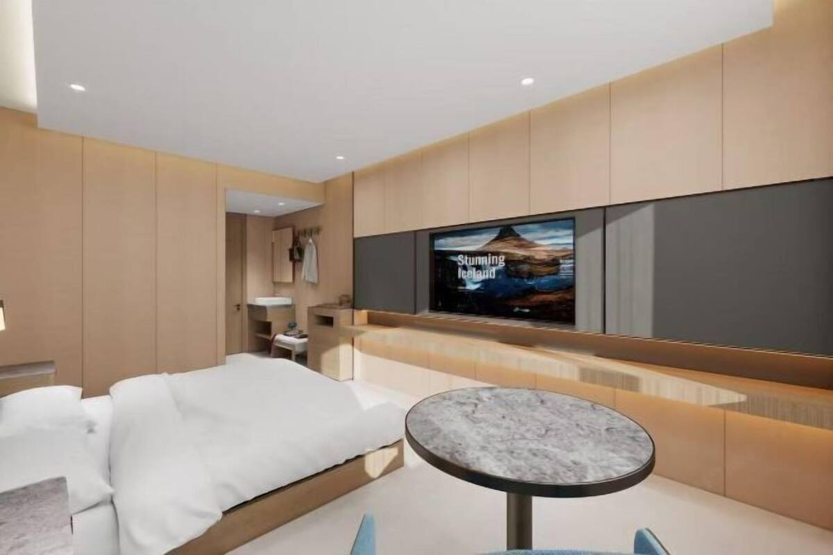 Moderni hotellihuone, jossa on sänky, pyöreä pöytä ja televisio, jolta näkyy ohjelma nimeltä ”Upea Islanti”.