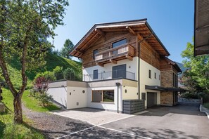 Una casa moderna de dos pisos con fachada de madera, un balcón y un camino de acceso a un garaje.