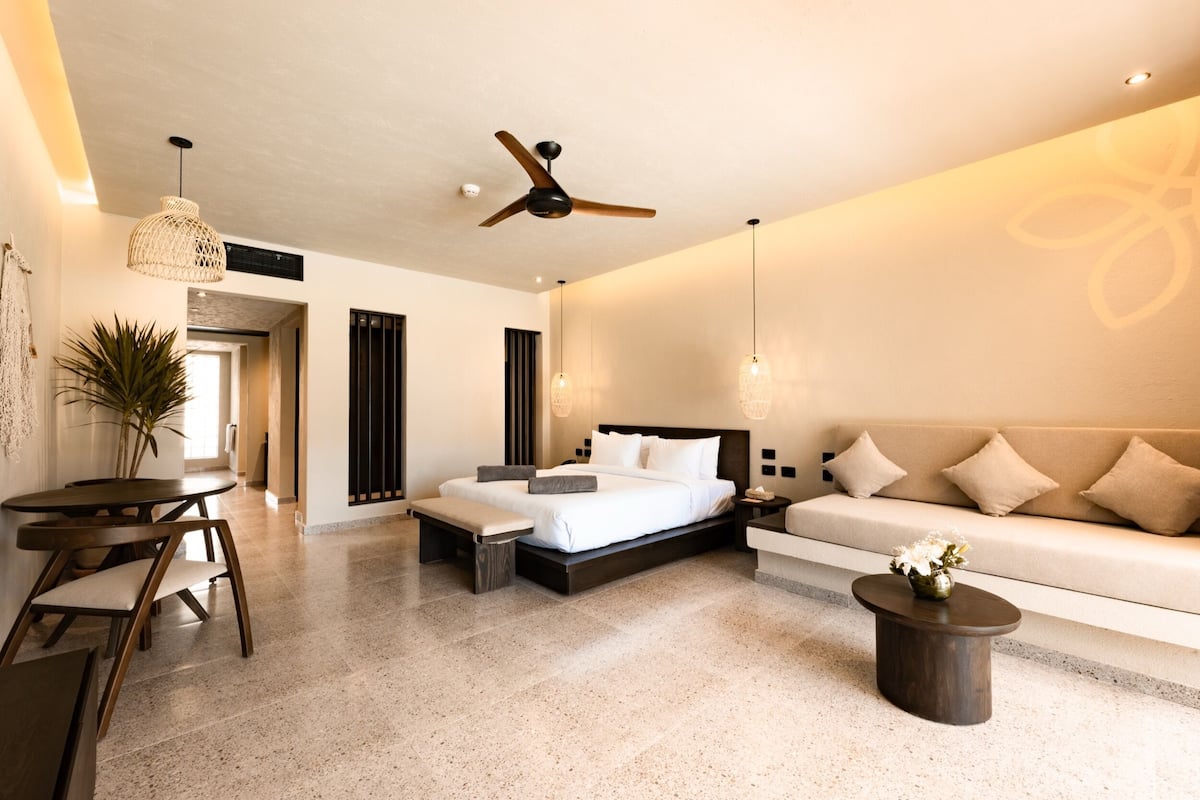 A modern bedroom with a bed, a sofa, a dining table, and a ceiling fan.