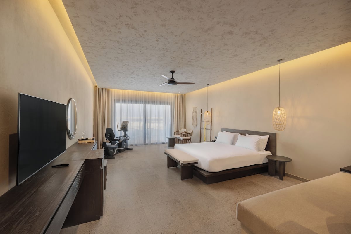 A modern hotel room with a large bed, a TV, exercise equipment, and a desk.