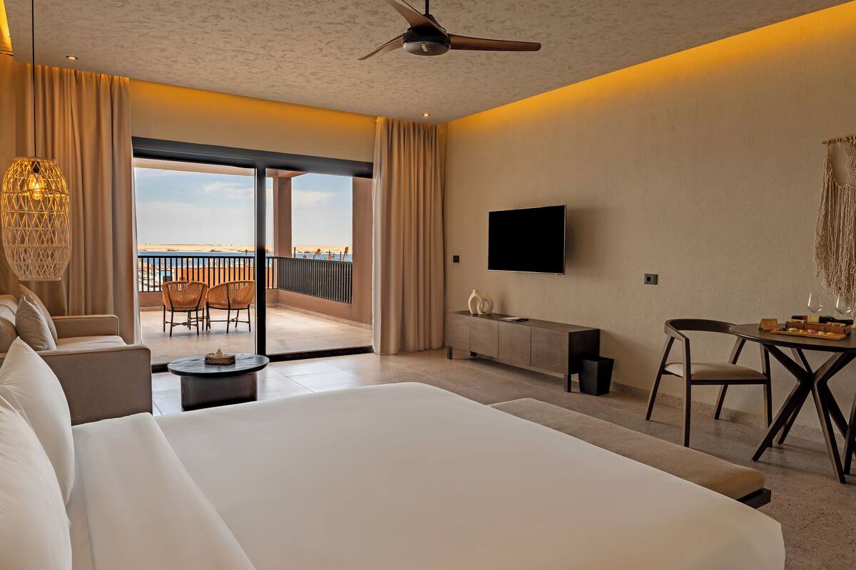 A hotel room with a large bed, a TV, a balcony with a view, and a dining area.
