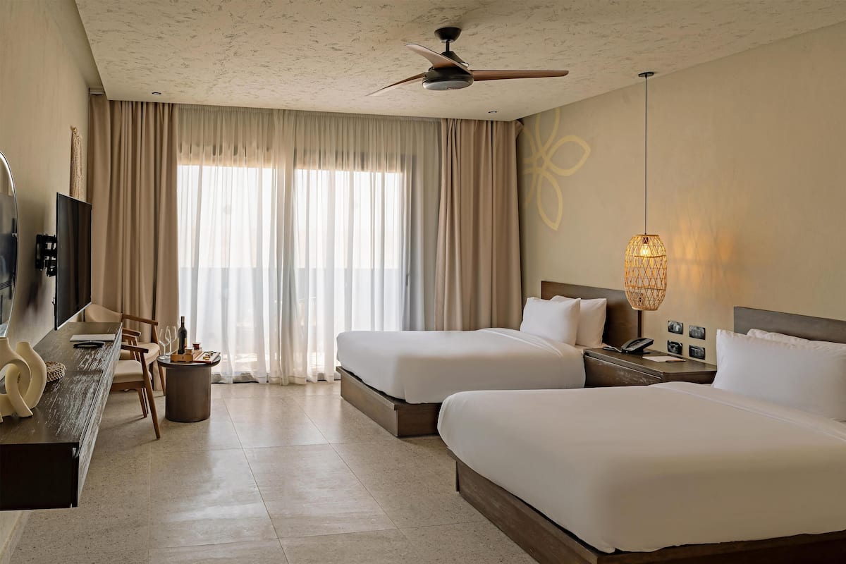 A hotel room with two beds, a desk with a chair, a television, and a ceiling fan.