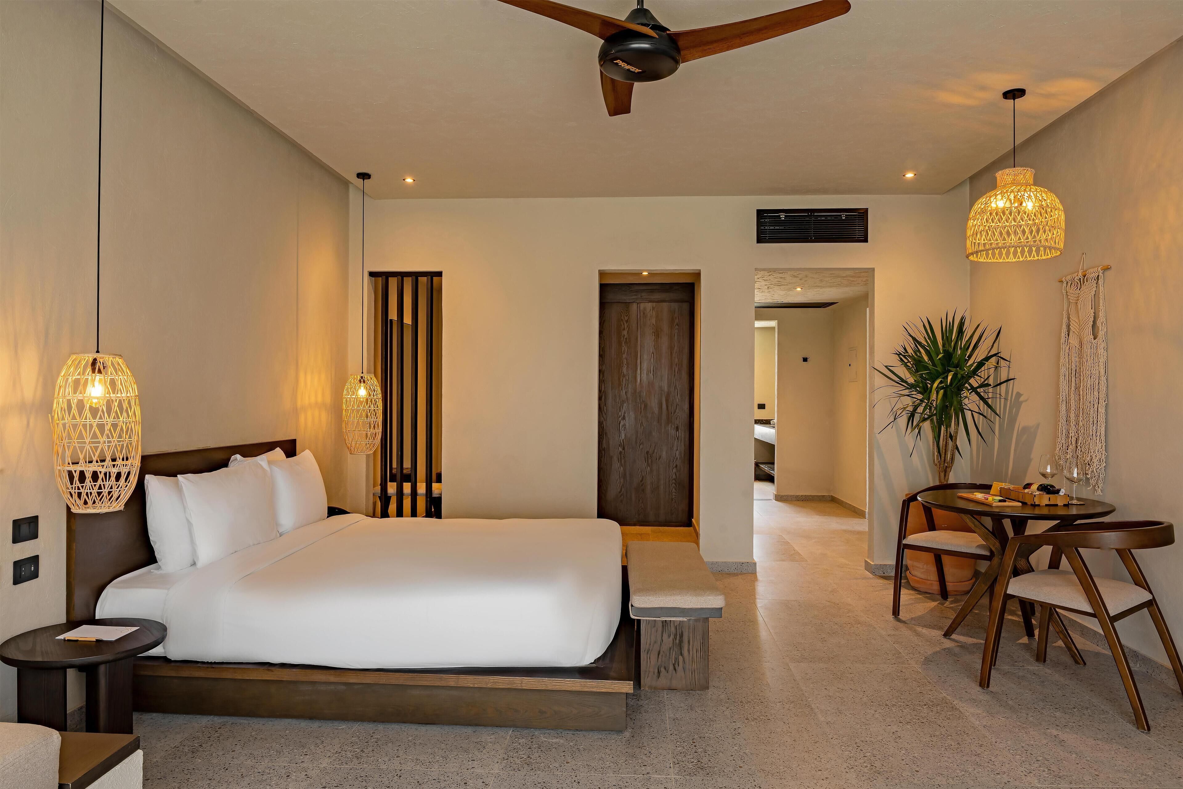 Ein modernes Hotelzimmer mit einem großen Bett, Nachttischen, einem Deckenventilator und einem Essbereich mit Tisch und Stühlen.