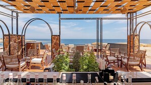 A beachside patio with wooden furniture, a bar area, and a view of the ocean. - Sentido Naga Bay (Soma Bay)