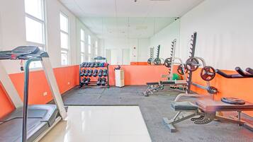 Un gimnasio con cinta de correr, estantes para pesas y varios equipos de ejercicio.