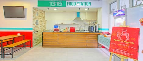 A food station with a counter, wooden benches, and a red signboard.