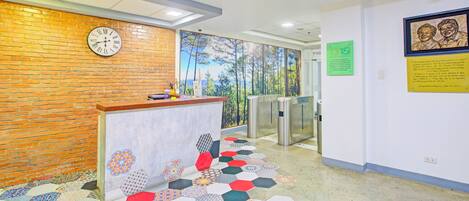 A reception area with a brick wall, a clock, a desk, a patterned floor, and a mural of trees.