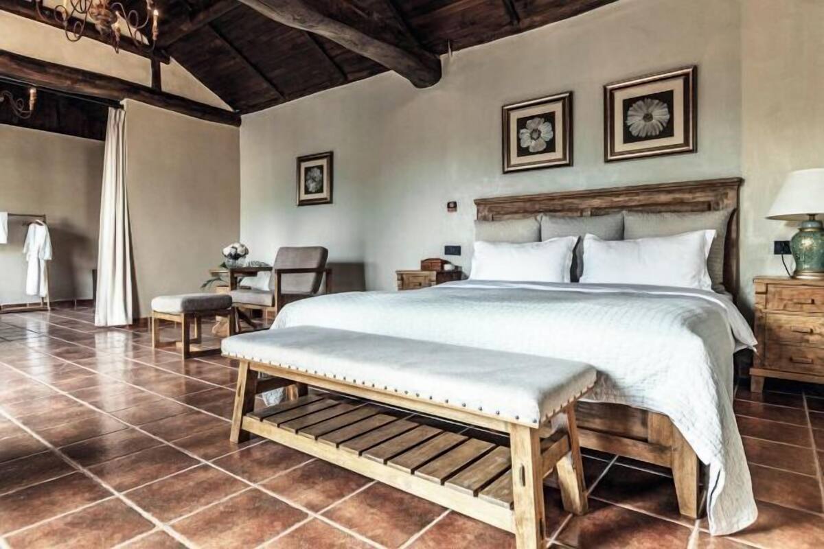 A bedroom with a large bed, wooden bench, and a rustic ceiling.
