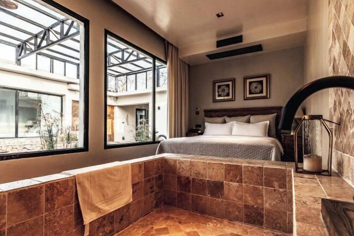 A modern hotel room with a large bed, a bathtub, and a view through a skylight.