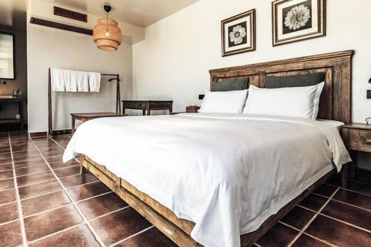 A bedroom with a large bed, wooden headboard, and a tiled floor.