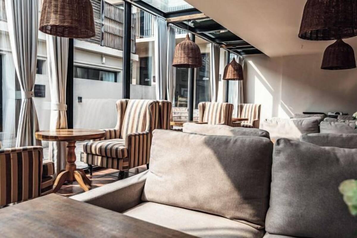 A modern lounge area with striped sofas, a round wooden table, and hanging wicker lamps.