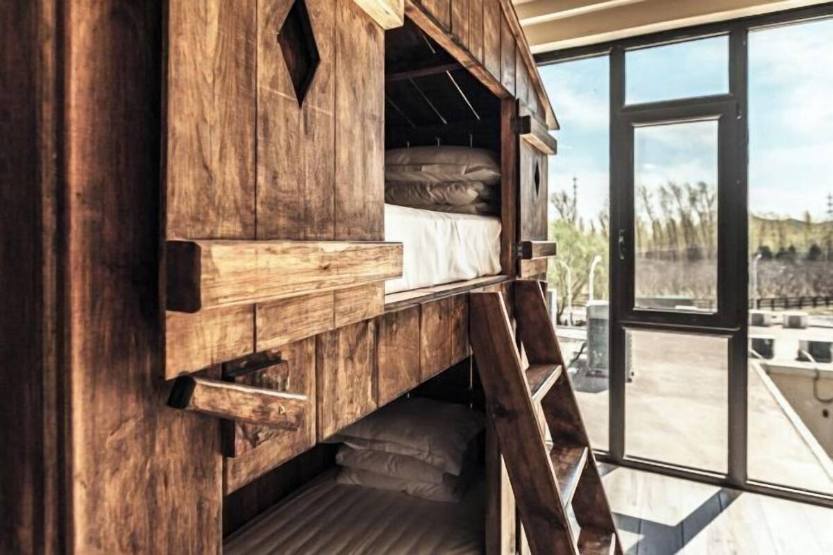A wooden bunk bed with a ladder, a window, and a view of the outdoors.