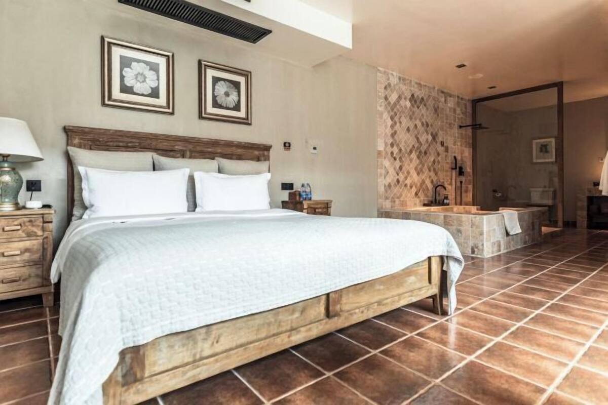 A bedroom with a wooden bed, a nightstand, a wall-mounted lamp, and a bathroom with a shower and bathtub.