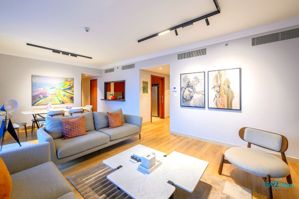Un salon moderne avec un canapé gris, une table basse et un fauteuil. Des œuvres d’art ornent le mur, et un coin repas est aménagé avec une table et des chaises.