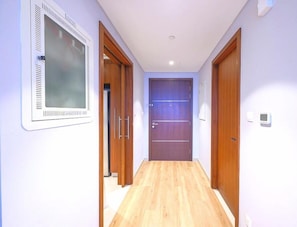 A hallway with wooden flooring, a door with a window, and a wall-mounted thermostat. - WYZ RENT|Unobstructed Burj Khalifa Views 3.5 Beds (Dubai)