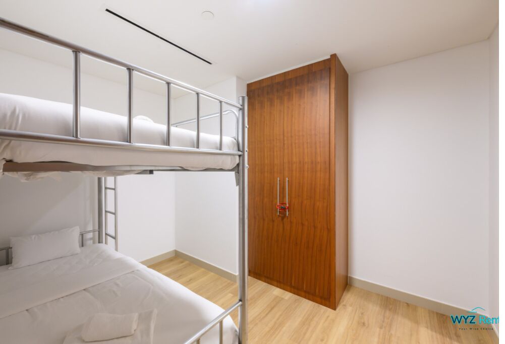 A dorm-style room with bunk beds, a wooden wardrobe, and a small window.