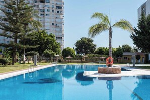 A swimming pool with a lifebuoy sculpture, surrounded by trees and a multi-story building in the background. - Vistas al Mar, Piscina, Parking, 900 m Playa, Wifi (Torremolinos)