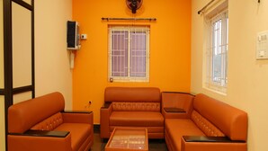 Una habitación con paredes naranja, un ventanal con barrotes, un ventilador de techo y dos sofás.