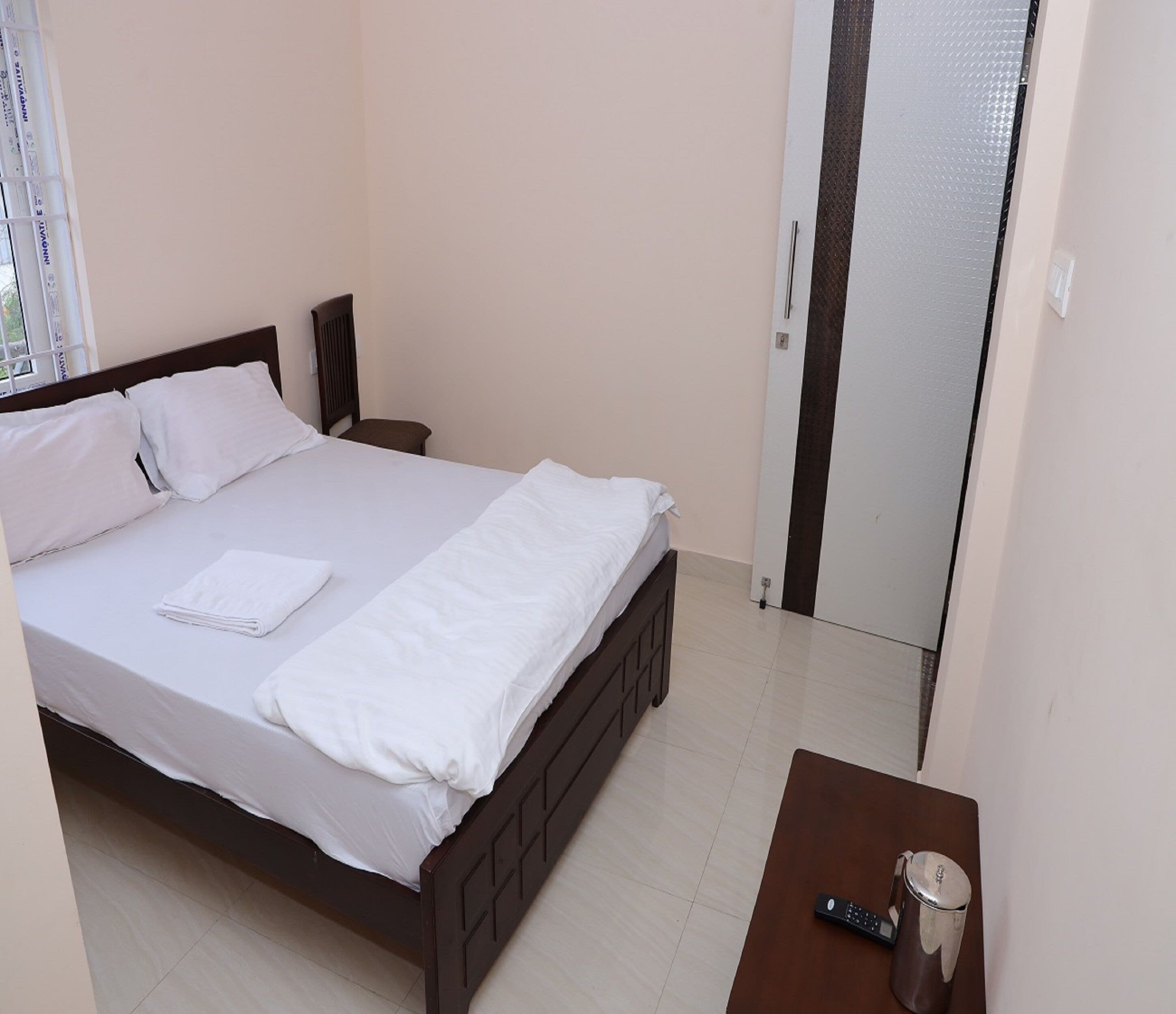 A neatly made bed with white linens, a bedside table with a remote control, and a door leading to another room.