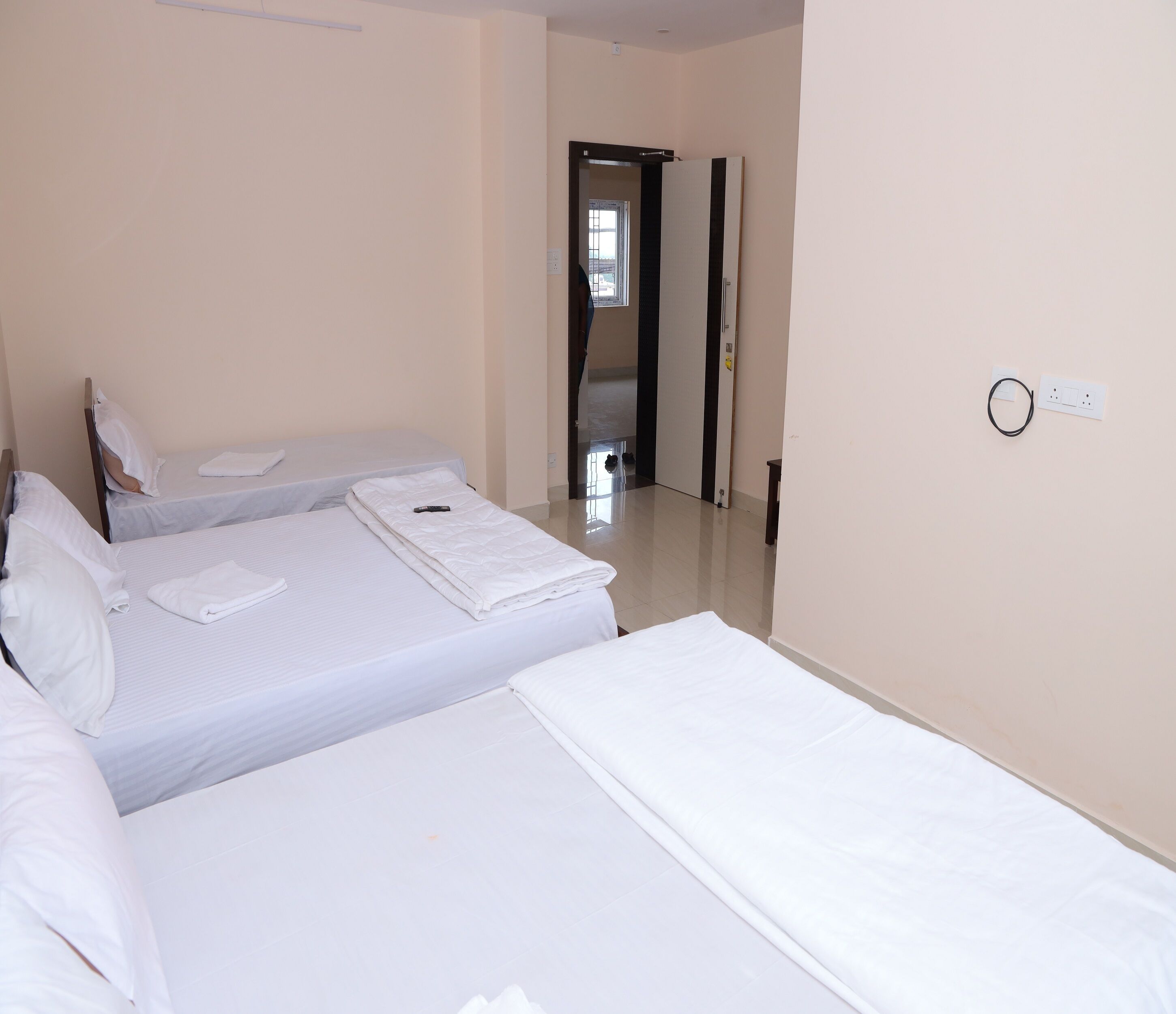 Ein Hotelzimmer mit drei Einzelbetten, einer zur Korridor führenden Tür und einer Steckdose an der Wand.