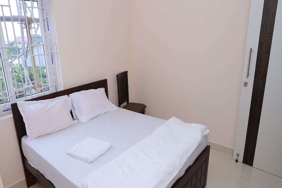 A neatly made bed with white linens, a wooden headboard, and a window with bars.