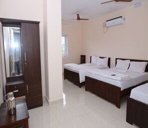 A hotel room with two beds, a wardrobe, a desk with a kettle, a ceiling fan, and an air conditioning unit. - Hotel Suryaa Grand (Vanur)