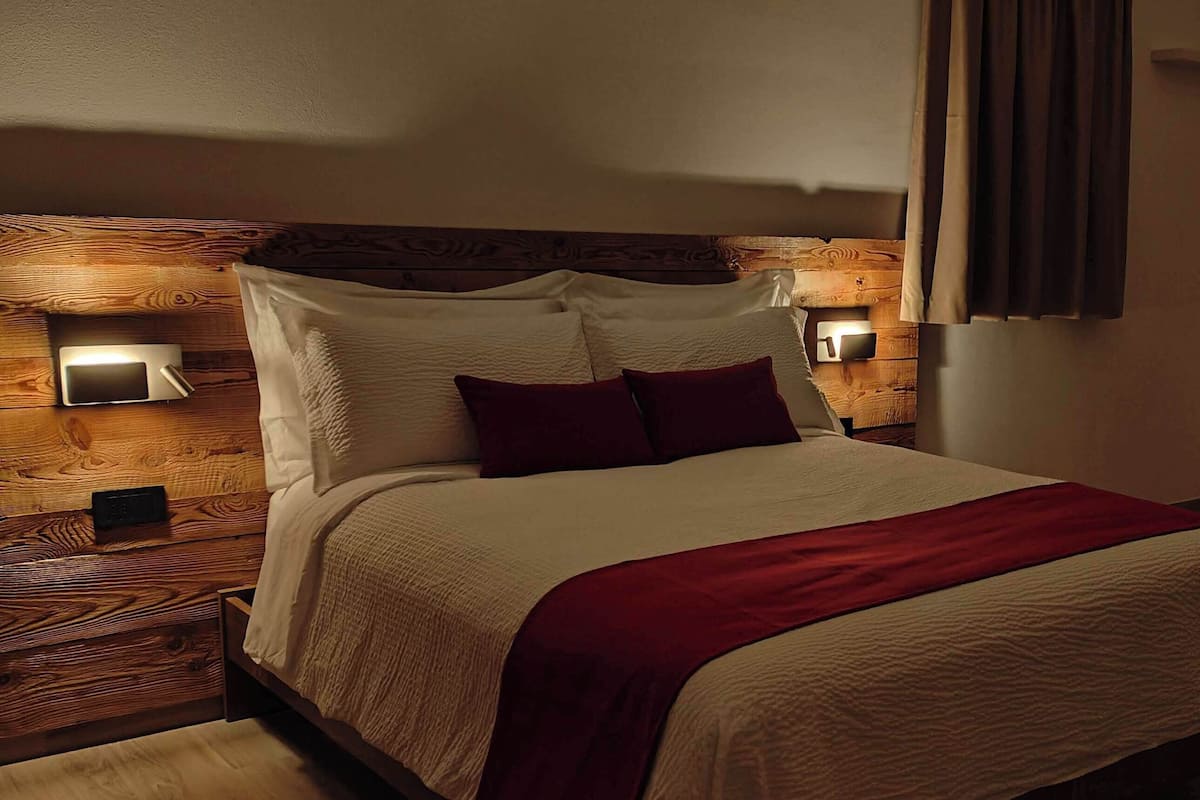 Een moderne slaapkamer met een houten hoofdbord, een groot bed met wit en rode beddengoed, twee wandlampen voor het lezen en een houten vloer.