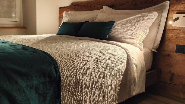 Una cama bien hecha con una manta color turquesa, almohadas blancas y una colcha beige con textura.