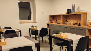 Un comedor moderno con mesas y sillas de madera, una encimera con electrodomésticos de cocina, y un ventanal que proporciona luz natural.
