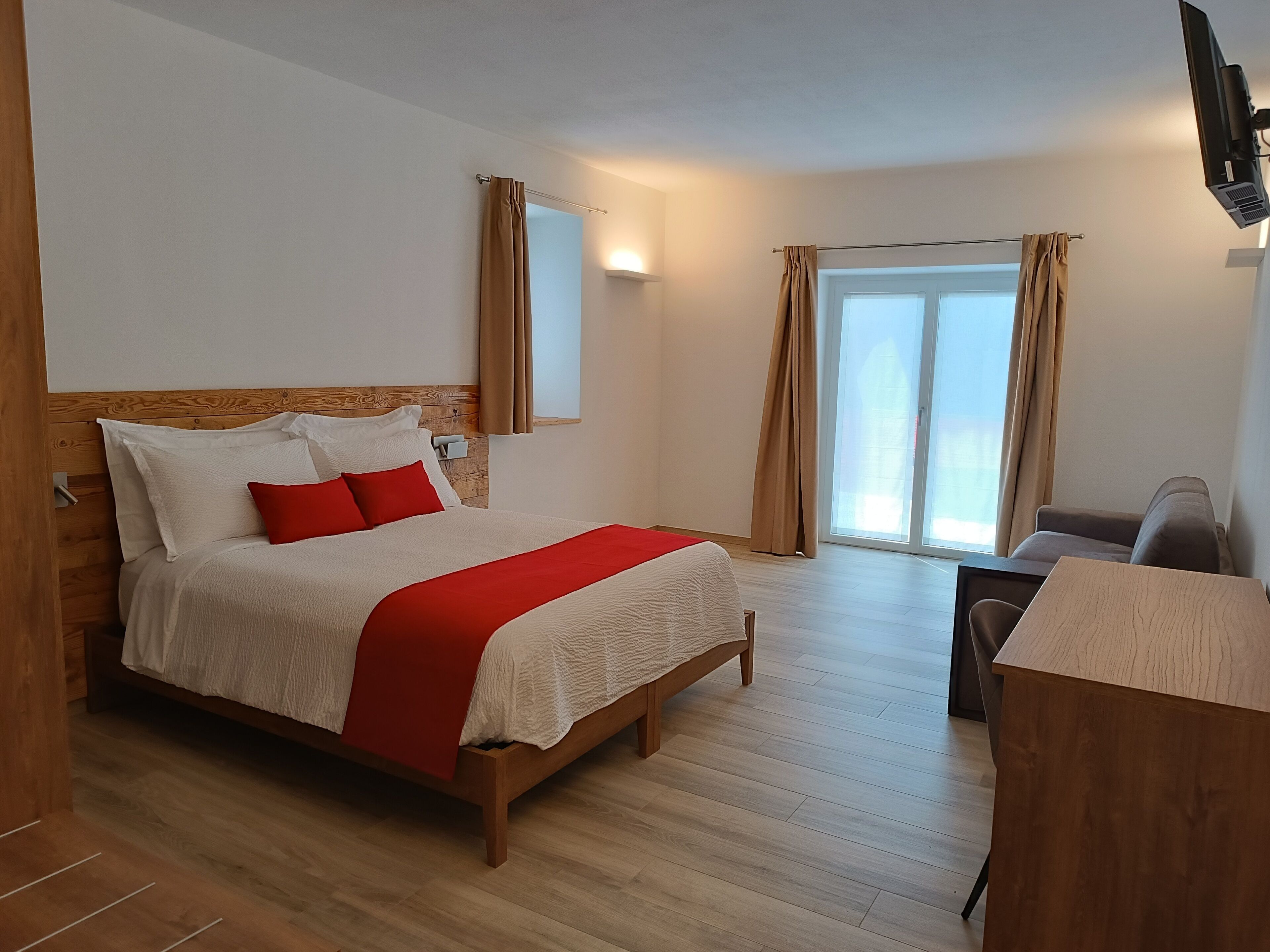Una habitación de hotel con una cama de madera, un escritorio, una silla y un ventanal con cortinas.