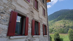 Un edificio de piedra con contraventanas rojas y vista a una ladera verde.