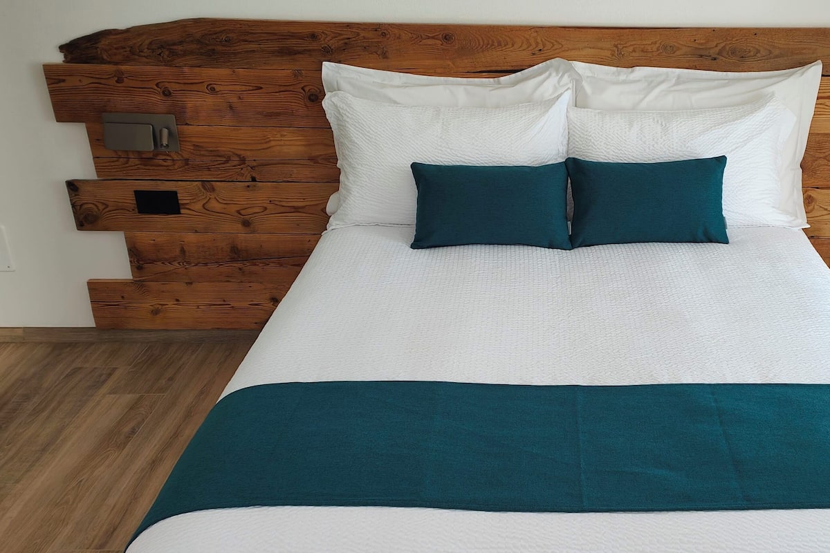 Een bed met witte beddengoed en teal gekleurde kussens, een houten hoofdbord en bedlampen.