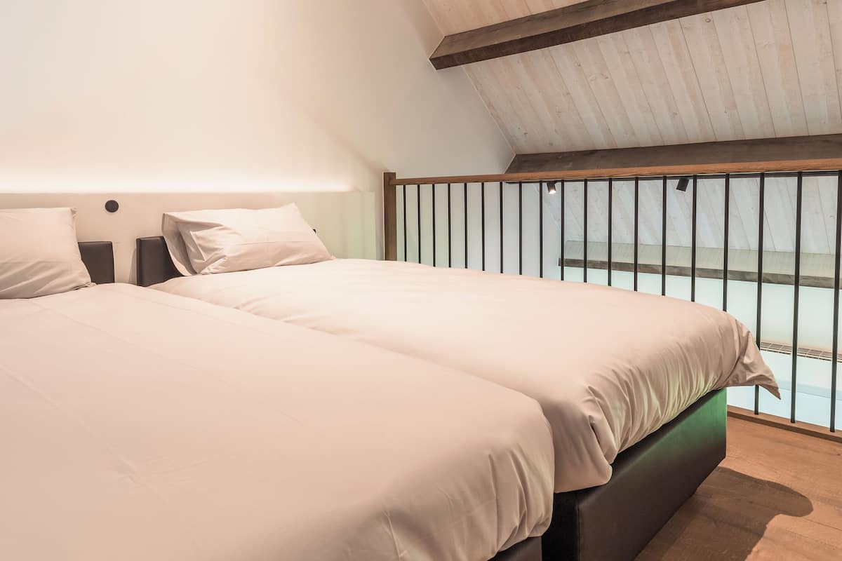 A bedroom with two beds, wooden beams on the ceiling, and a view through a window.