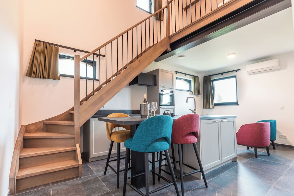 A modern kitchen with a wooden staircase, a dining area with colorful chairs, and a kitchen island.