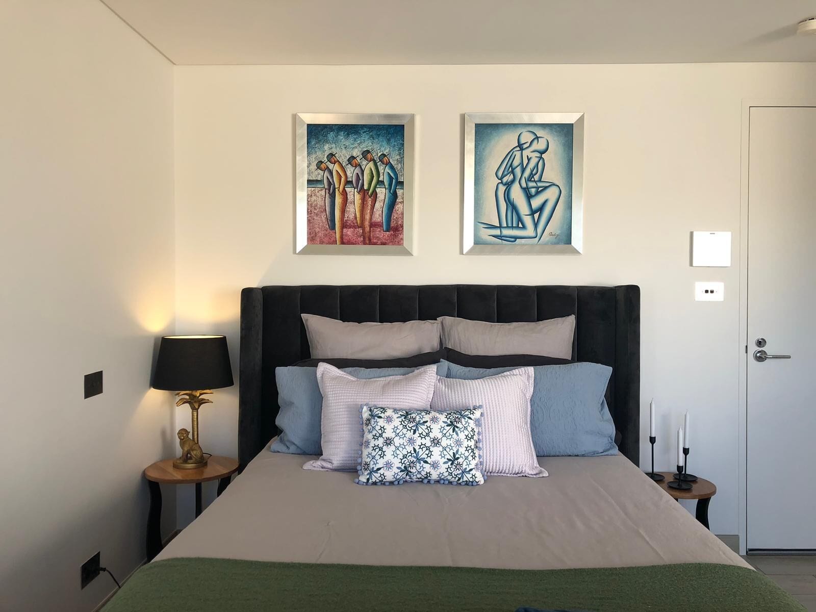 Une chambre à coucher avec un grand lit, une table de chevet avec une lampe et deux œuvres d’art encadrées accrochées au mur.