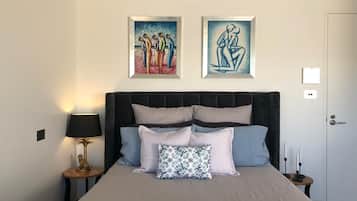 Une chambre à coucher avec un grand lit, une table de chevet avec une lampe et deux œuvres d’art encadrées accrochées au mur.