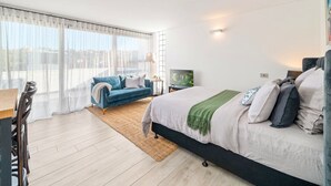 A modern bedroom with a large bed, a blue sofa, and a view of the city through large windows. - La Casa De Frida  (Bondi Beach)