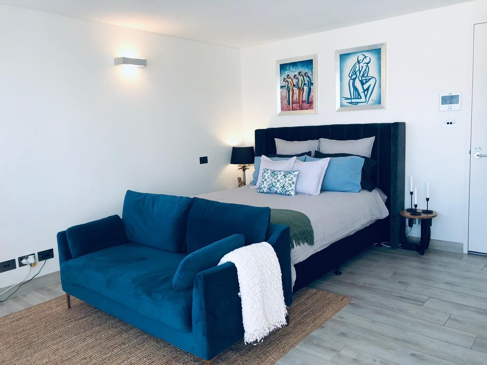 Un dormitorio moderno con una cama, un sofá azul y dos obras de arte colgadas en la pared.