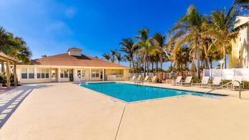 A pool area with lounge chairs, a building with a red roof, and palm trees.