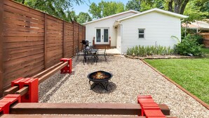 A backyard with a wooden deck, a fire pit, and a small white house.