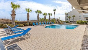 A pool area with lounge chairs, palm trees, and a building in the background. - Pelican Landing Unit 330 - Ocean view (Myrtle Beach)