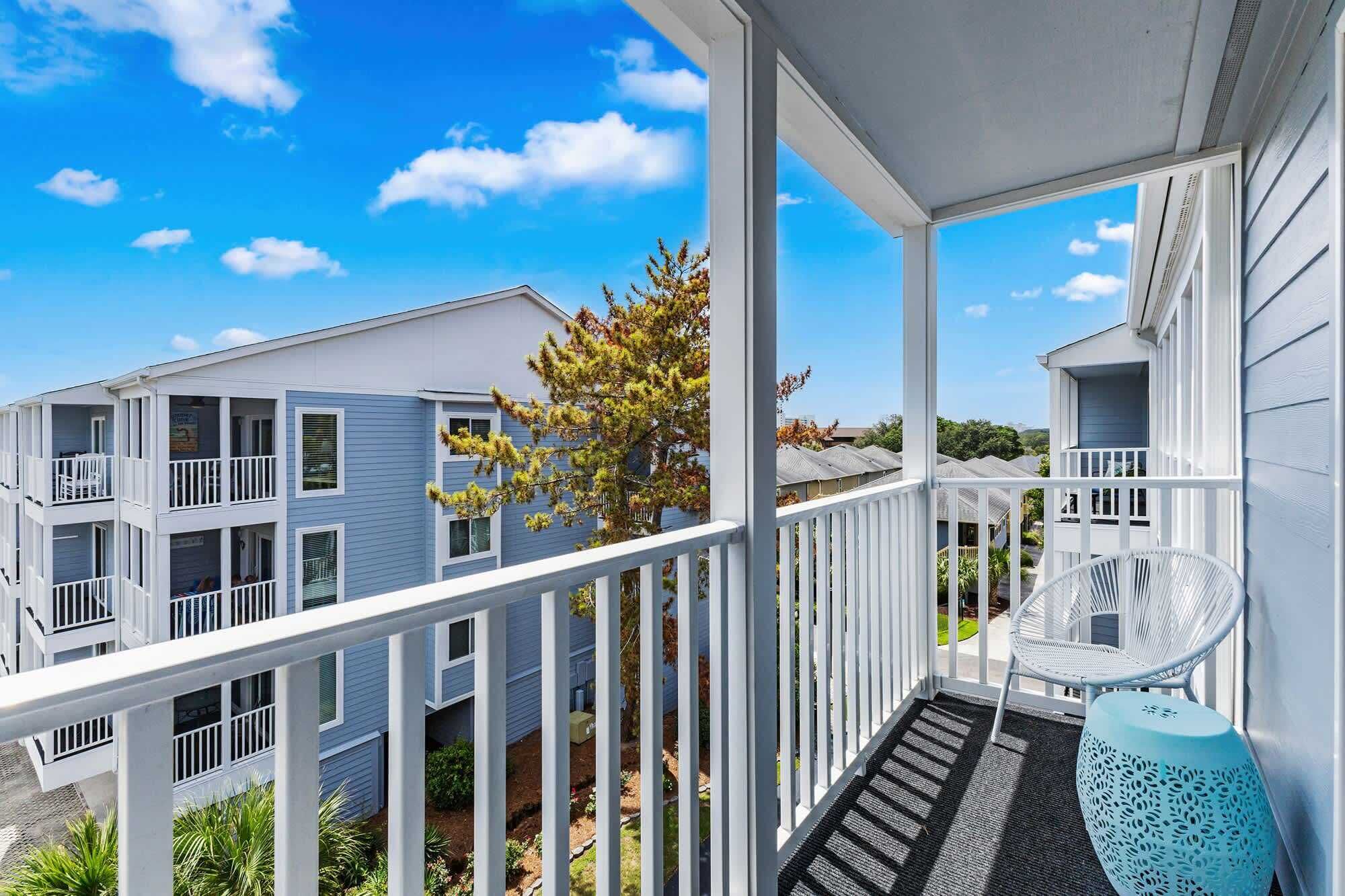 A multi-story building with balconies, a covered porch, and a view of neighboring houses.