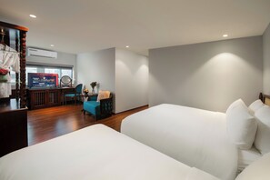 A hotel room with two beds, a desk with a computer, a chair, and a small table with a vase. - Serene Central hotel (Hanoi)